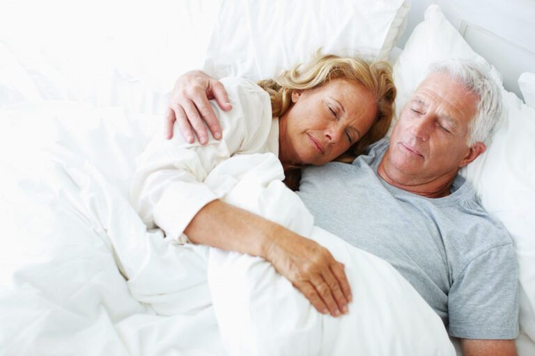 Un homme et une femme sont allongés ensemble sur le lit. La femme est allongée la tête sur la poitrine de son mari.