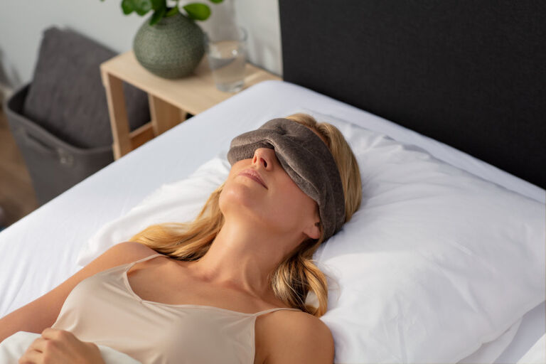Une femme est allongée sur le dos, la tête sur un oreiller Original. Elle porte un masque de sommeil.