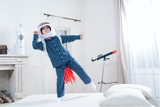 Un enfant debout sur un lit et habillé en astronaute.